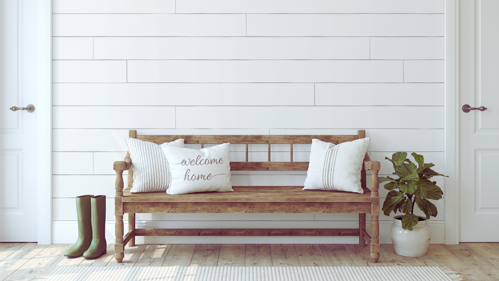 Entry way with wooden bench, "welcome home" pillow, a potted plant and rubber boots.