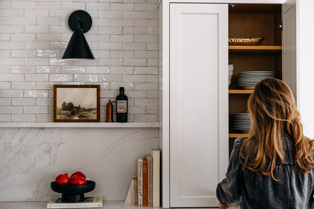 Kitchen with glazed white brick tile, a black cone sconce, a marble backsplash and ledge, and an open pantry cabinet